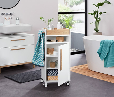 Im Badezimmer stehen ein weißer Waschbeckenunterschrank »Eklund« mit zwei Schubladen, ein Utensilo, ein Seifenspender, ein Frottier-Badetuch, 2 Jacquard-Handtücher, 2 Frottier-Handtücher (anthrazit), 2 Dosen aus Bambus, 2 LED-Dekosteine und ein Bad-Beistellwagen »Eklund«.