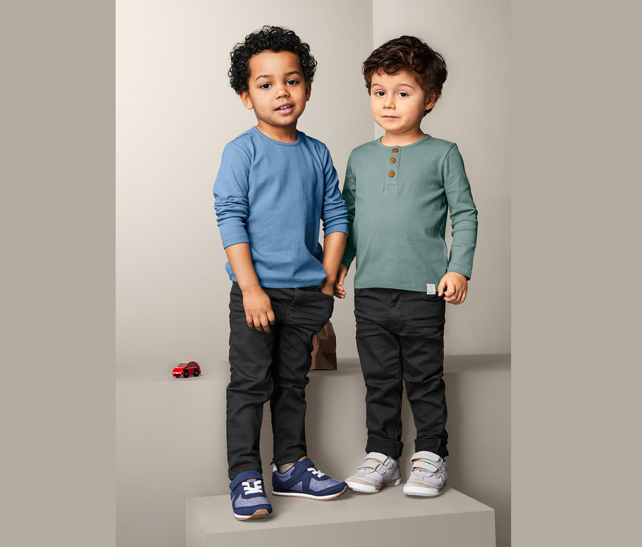 Zwei Jungen stehen nebeneinander und tragen 2 Langarmshirts und schwarze Hosen.