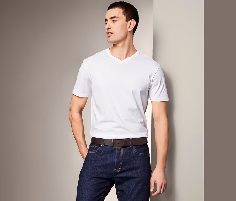 Mann posiert in Jeans und weißem T-Shirt mit Ledergürtel.