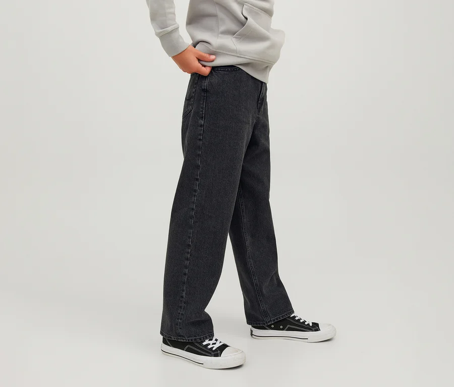 Person trägt schwarze Jack&Jones JJOrginial Alex Jeans, einen hellgrauen Hoodie und schwarz-weiße Sneaker, eine Hand hält den Hosenbund der Jeans.