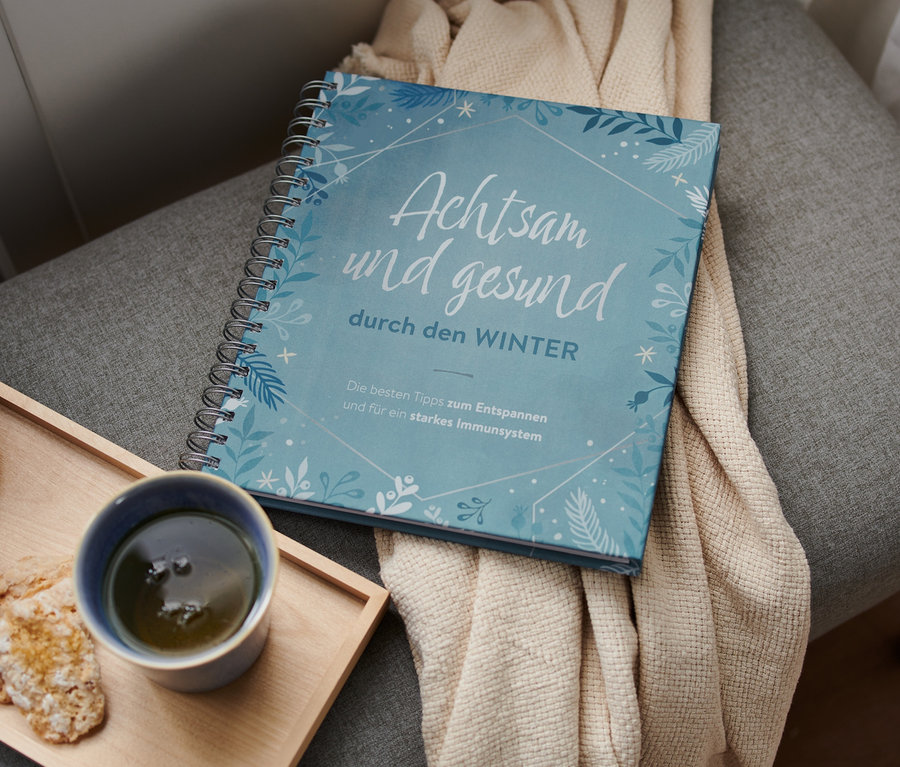 Das Buch »Achtsam und gesund durch den Winter« liegt auf einem grauen Hocker neben einer Tasse und Keksen.