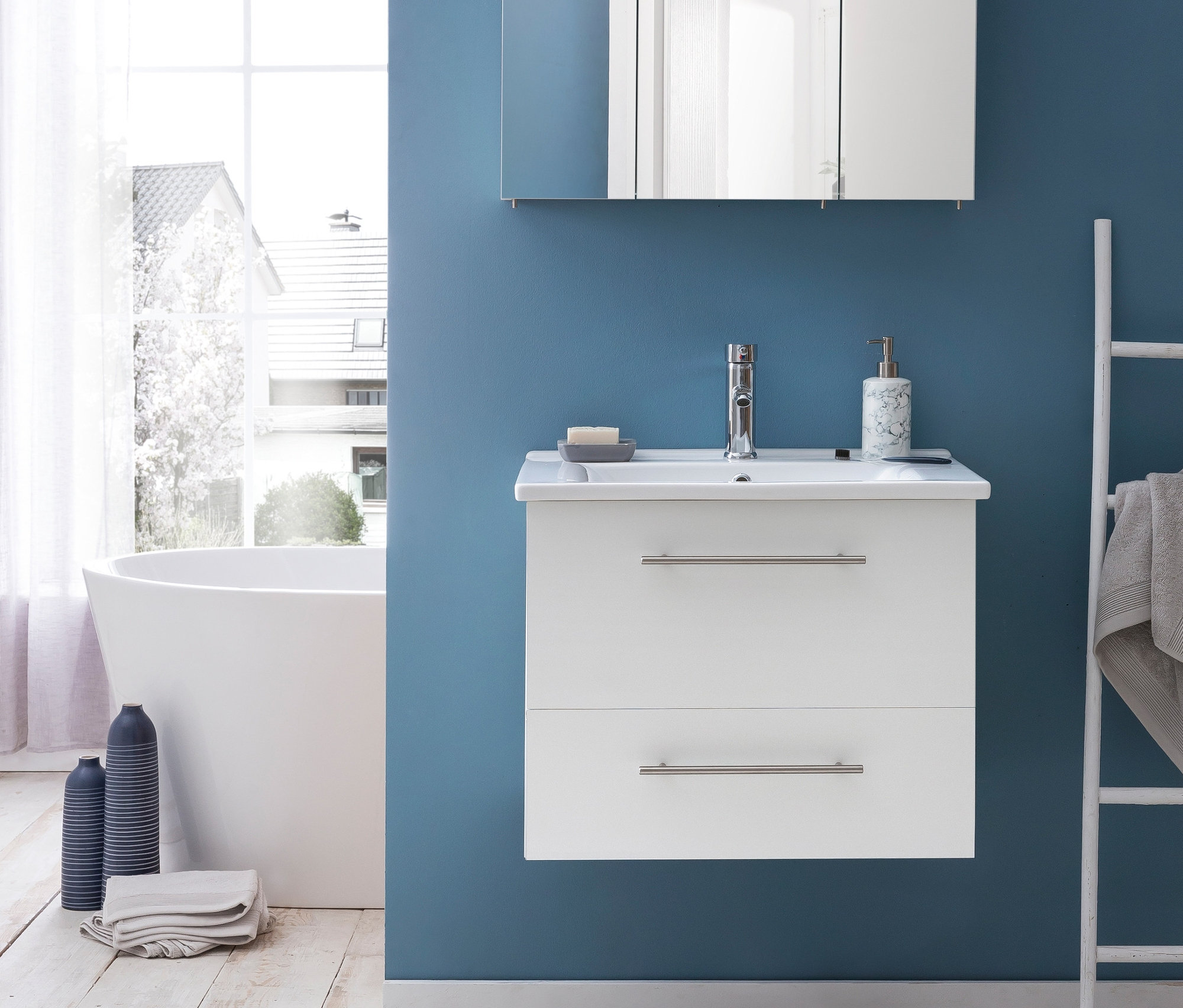 Ein Badezimmer mit einem weißen Waschtisch »Runa WT 650«, einem Spiegelschrank »Runa SPS Irene 800.1« in weißglänzend, einer Badewanne und einem Heizkörper.