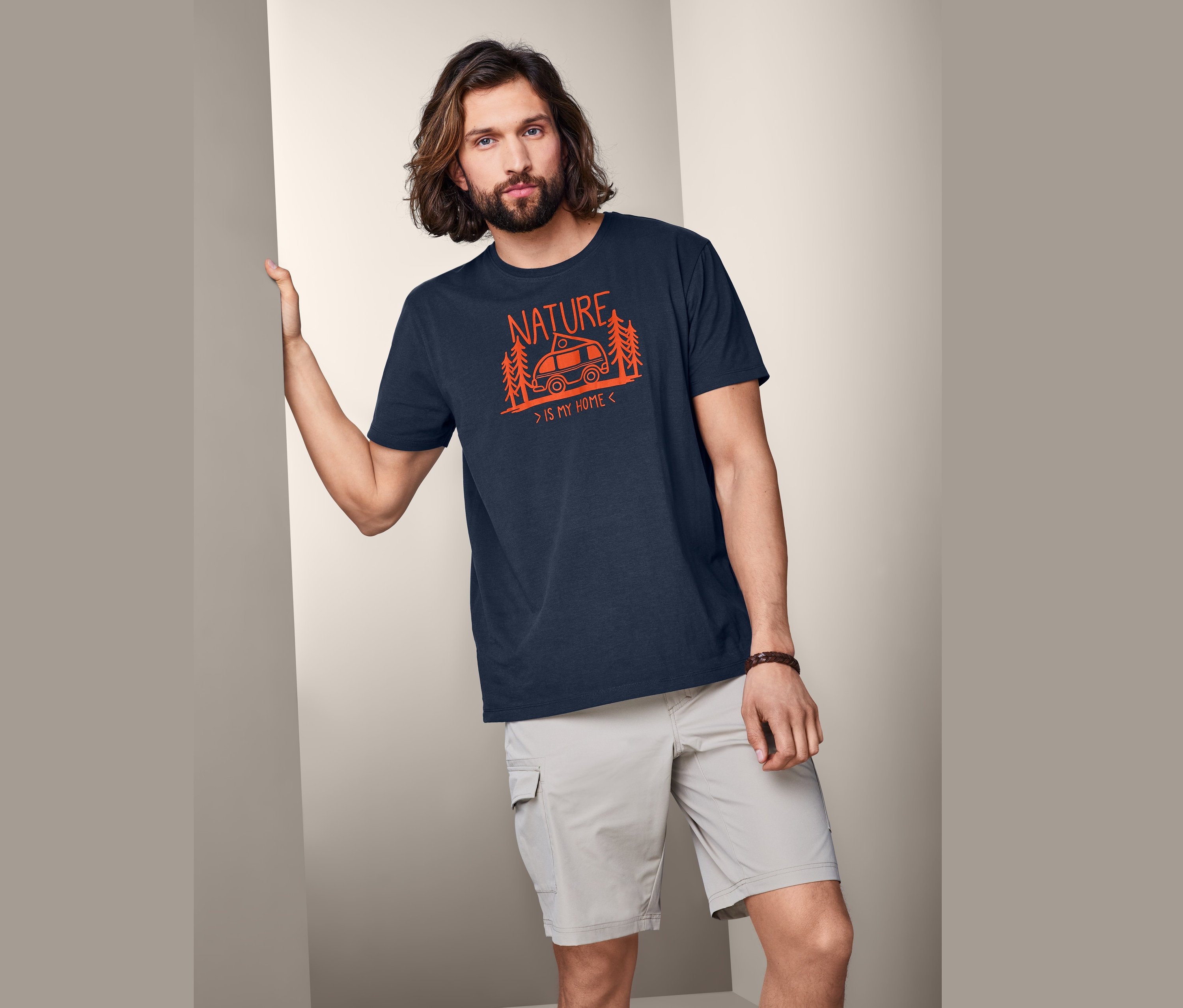 Mann posiert in marineblauem Funktions-T-Shirt mit orangefarbenem Aufdruck "Nature is my home".