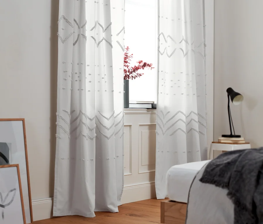 Zwei Vorhangschals mit geometrischen Mustern hängen an einem Fenster.