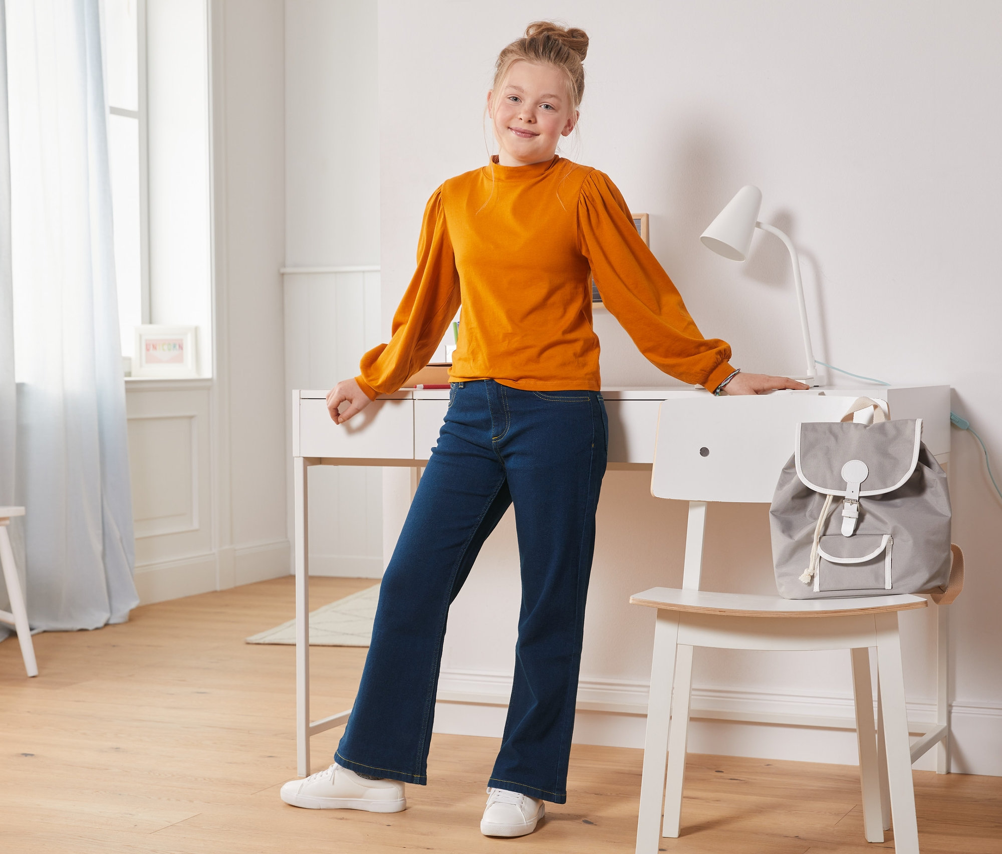 Mädchen steht am Schreibtisch und trägt eine Bootcut-Jeans.
