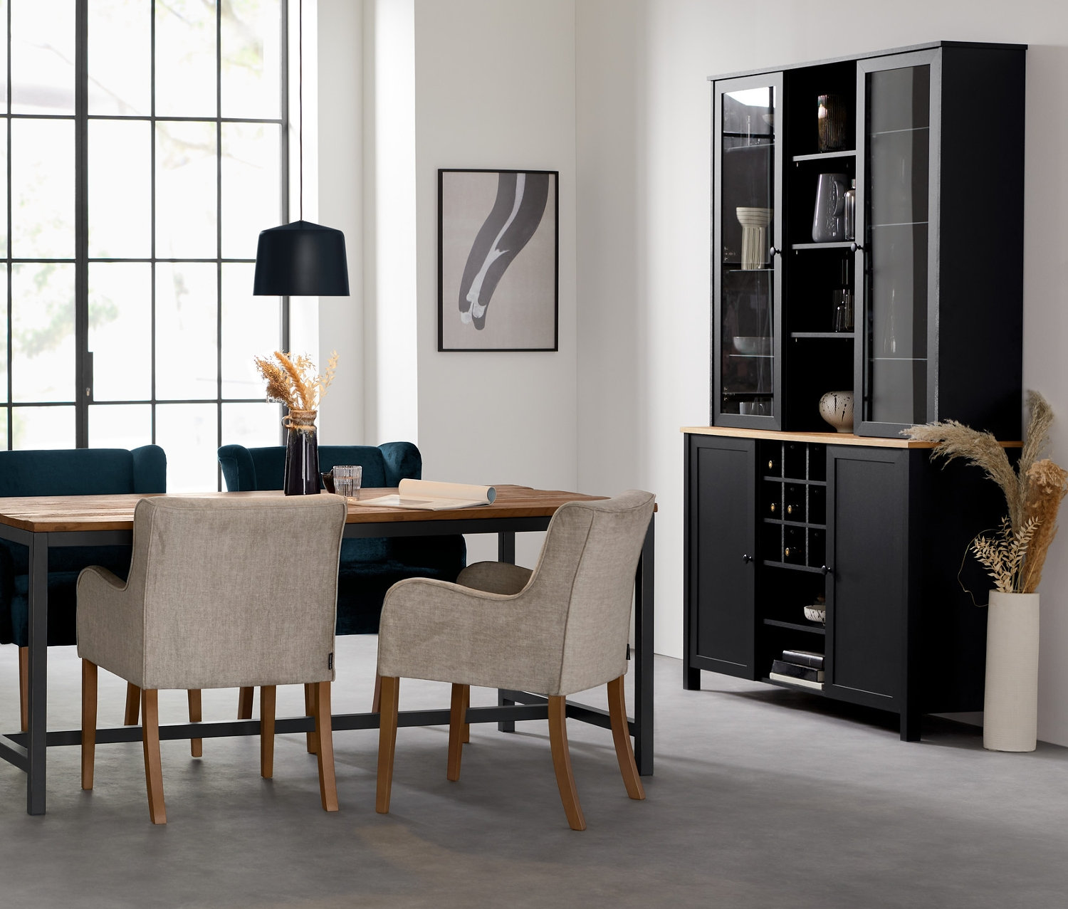 Ein Esszimmer mit einer schwarzen Hängeleuchte aus Metall über einem Actona Esstisch »Vintage« mit Polsterstühlen »Hendrick« und »Leopold«. Im Hintergrund steht ein Buffetschrank.