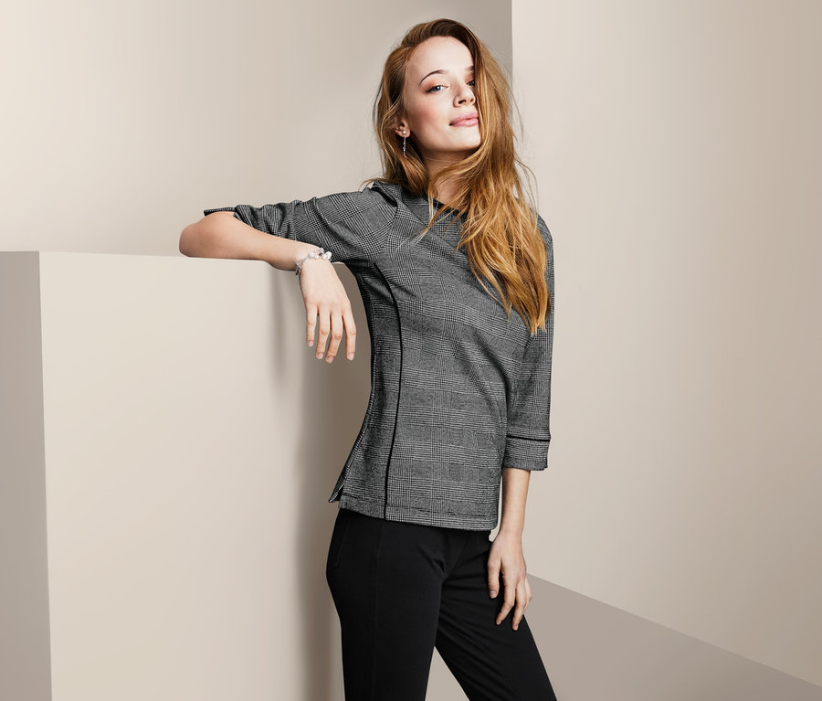 Frau posiert in einem Sweatshirt mit 3/4-Arm und einer schwarzen Hose.