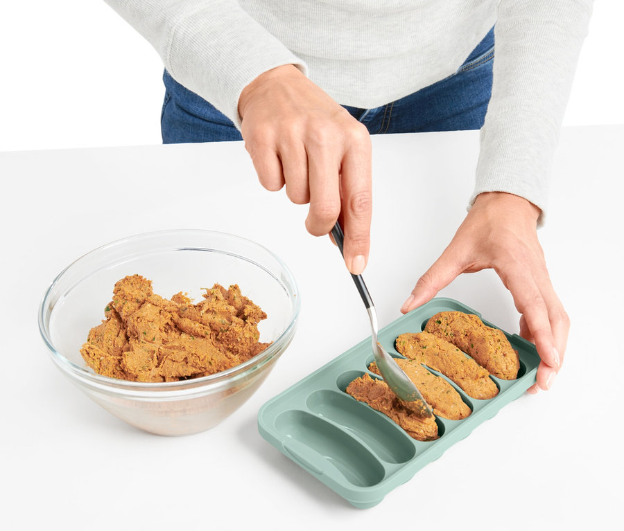 Frau füllt eine Mikrowellen-Veggie-Würstchen-Bereiter Form mit einer Mischung aus einer Glasschüssel.