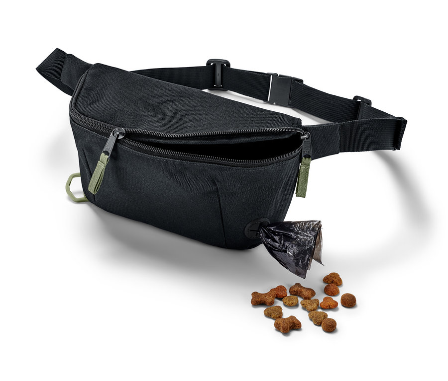 Eine schwarze Hunde-Gassitasche mit offenem Fach, aus dem Hundefutter herausfällt.