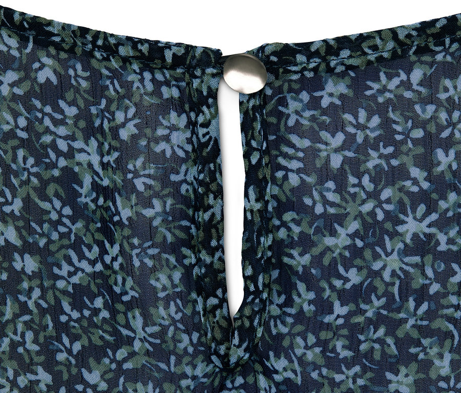 Detailaufnahme einer Tunika mit blau-grünem Blumenmuster und silberfarbenem Knopf.