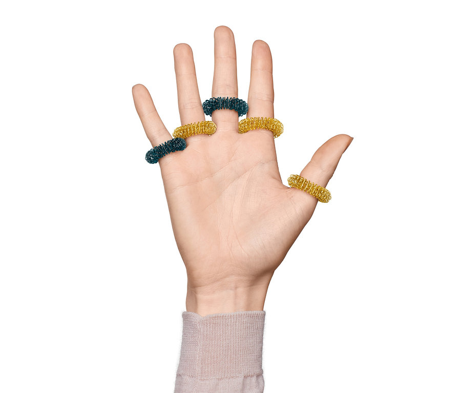 Hand mit Finger-Massageringen, zwei grün und drei gold.