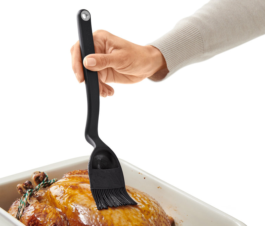 Eine Hand bestreicht ein gebratenes Huhn in einer Auflaufform mit einem Back-und-Braten-Pinsel.