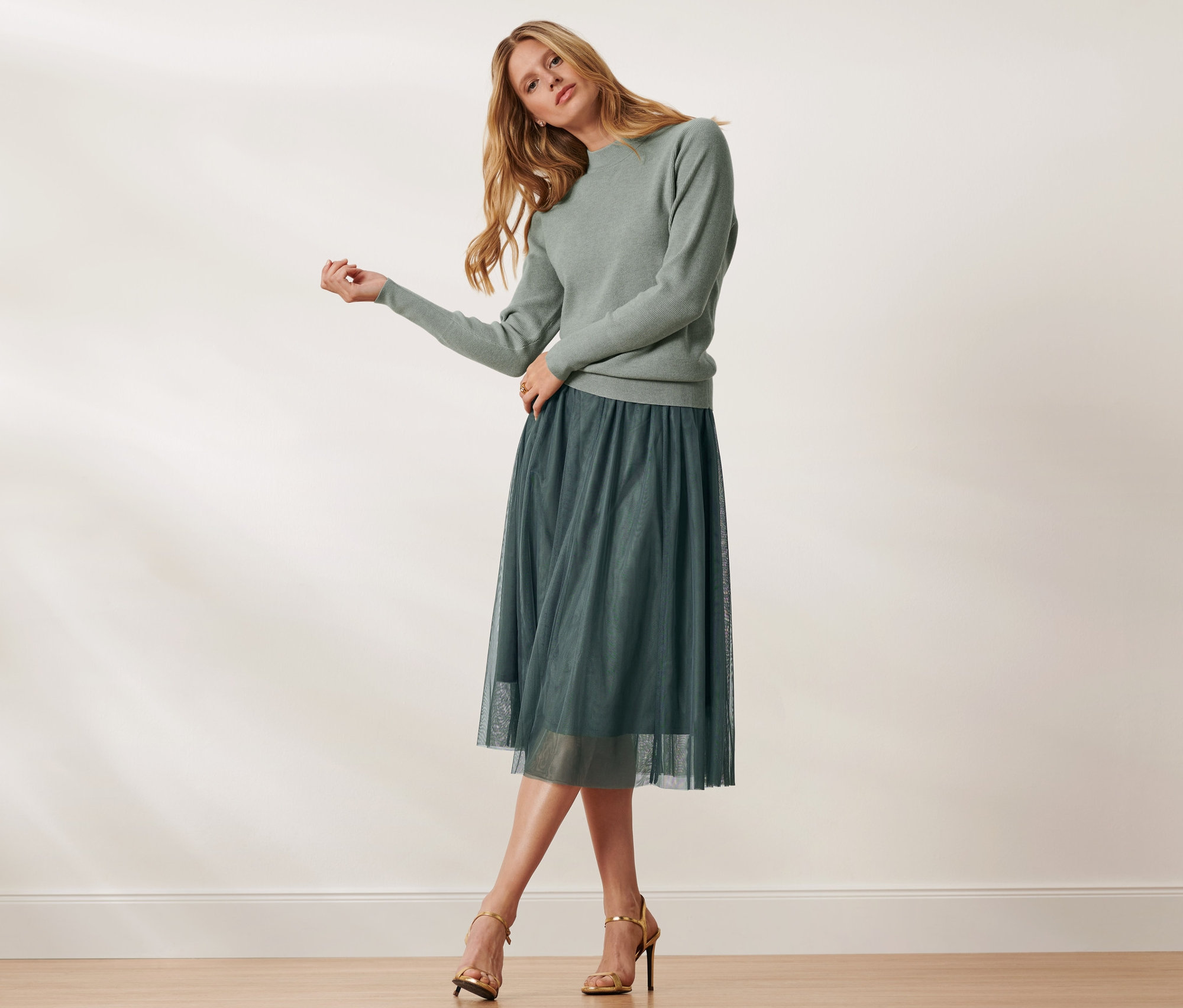 Frau posiert in grünem Pullover und Tüllrock.