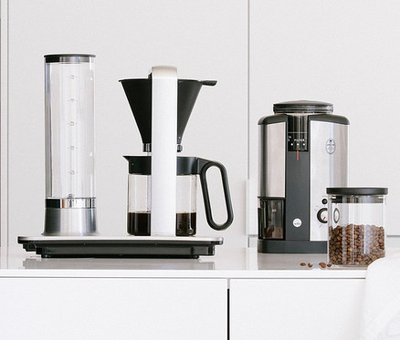 Auf einer weißen Anrichte stehen eine Wilfa Kaffeemaschine »Svart Precision« und eine Wilfa Kaffeemühle »Svart Nymalt«.