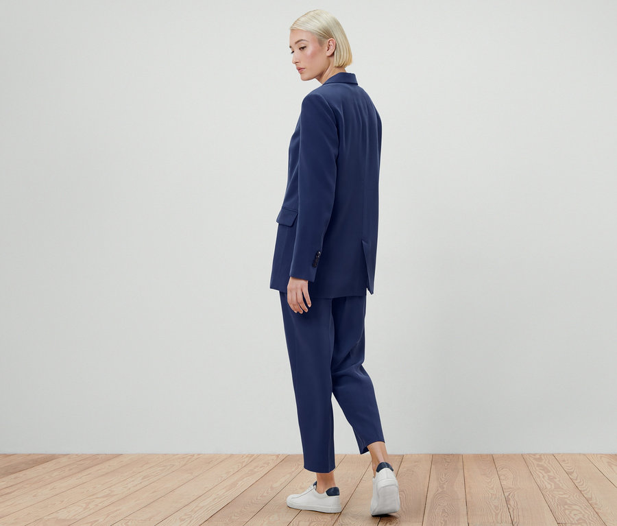 Frau posiert in Webblazer und Hose.