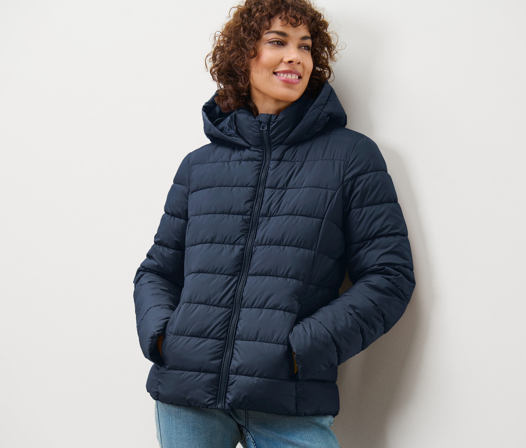 Frau lächelt und trägt eine dunkelblaue Steppjacke mit Kapuze.