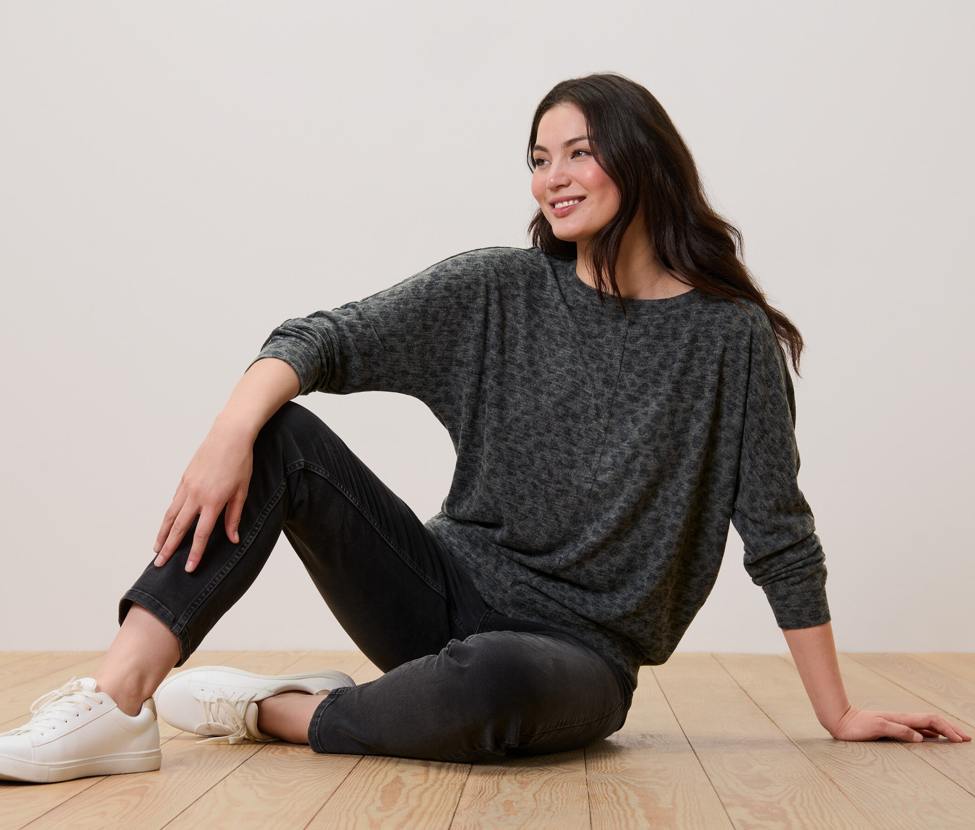 Frau sitzt auf dem Boden und trägt ein bedrucktes Fledermausshirt, schwarze Jeans und weiße Turnschuhe.