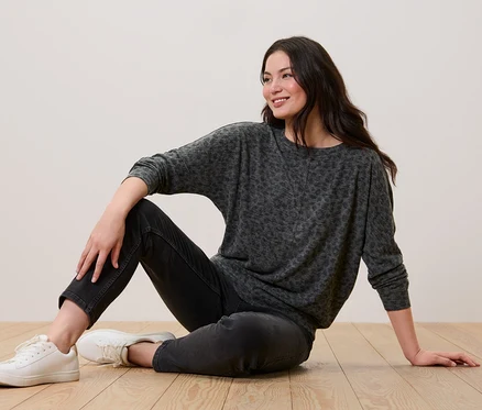 Frau sitzt auf dem Boden und trägt ein bedrucktes Fledermausshirt, schwarze Jeans und weiße Turnschuhe.