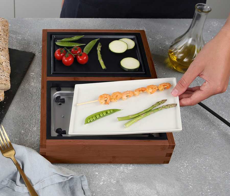 Person hält Teller mit Garnelen und Gemüse über Tischgrill "Dinner4All".