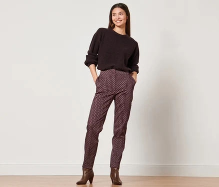 Frau posiert in braunem Pullover und Webhose.