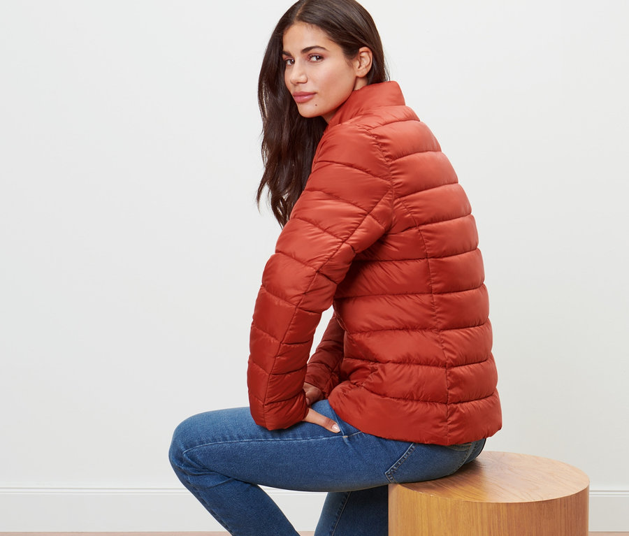 Frau sitzt auf einem Hocker und trägt eine orangefarbene Steppjacke.