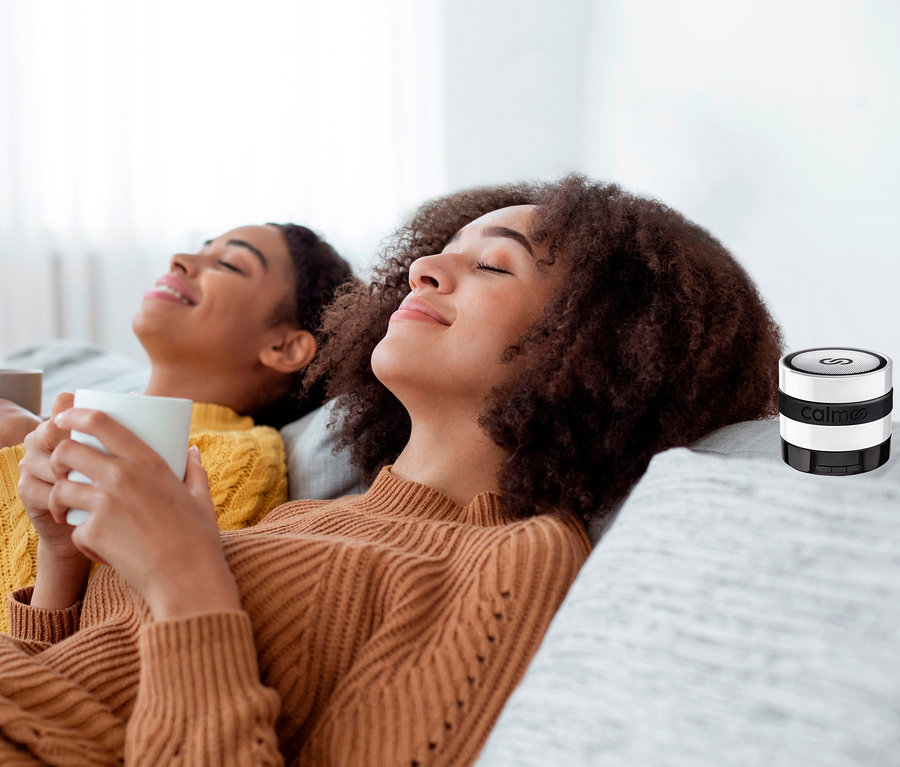 Zwei Frauen liegen entspannt mit Tassen auf einem Sofa neben einem calmoo Pure Relax System.