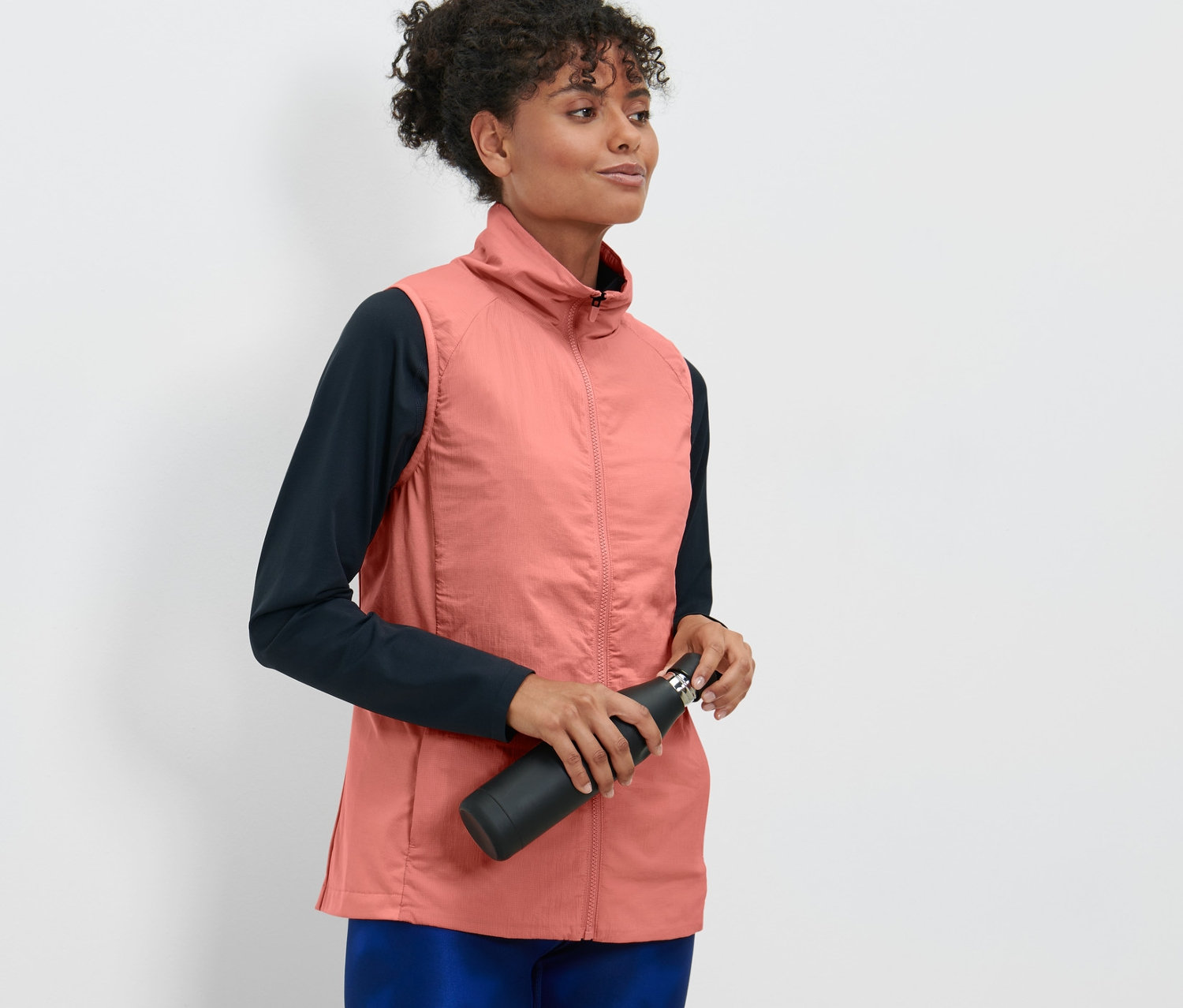 Frau hält eine schwarze Wasserflasche und trägt eine rosa Laufweste.