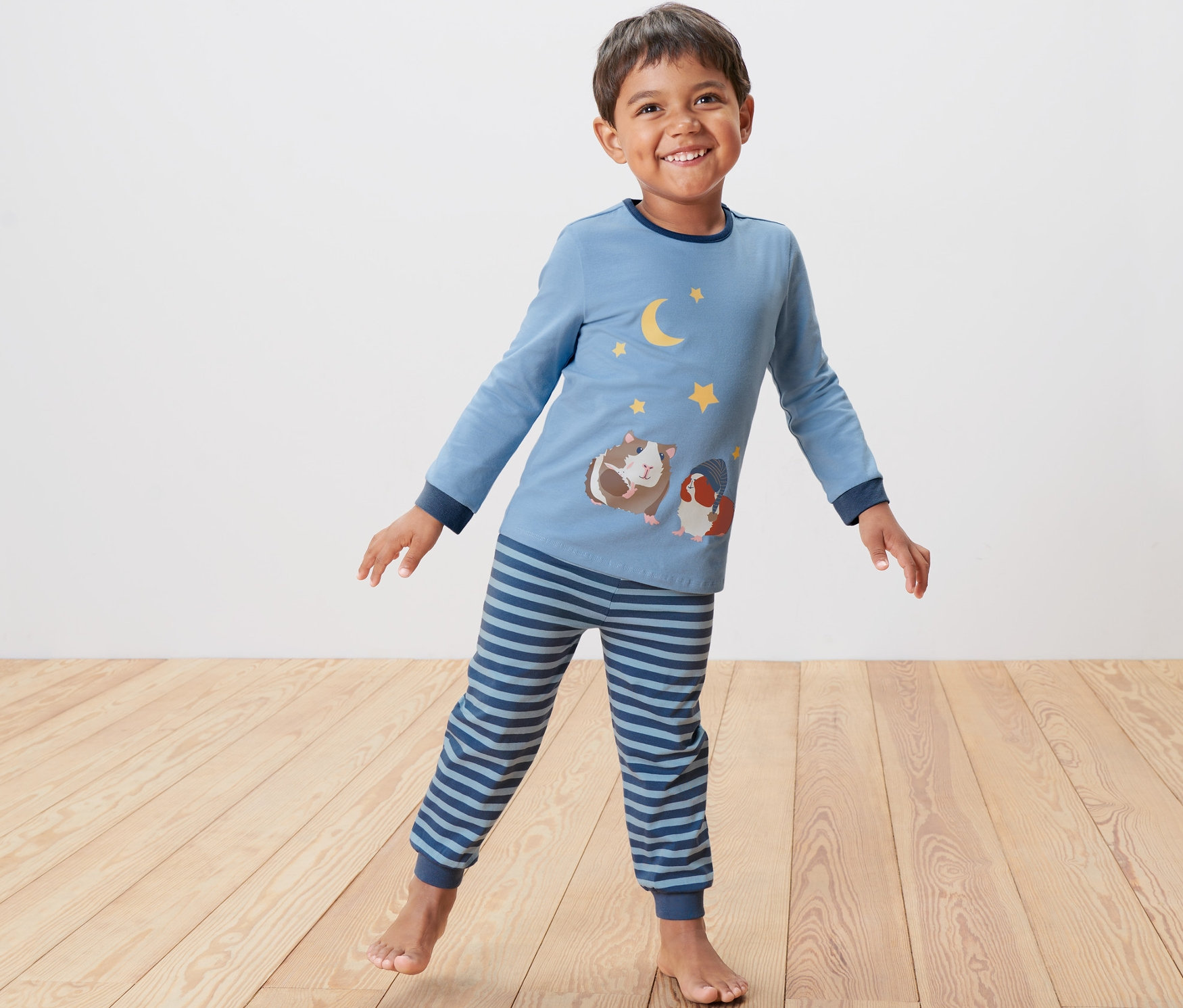 Junge steht und trägt einen blauen Kleinkind-Pyjama mit Meerschweinchen-Motiv.