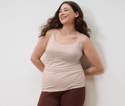 Frau posiert in 3 Hemdchen und Pyjamahose.