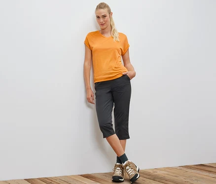 Frau lehnt an Wand und trägt oranges Funktionsshirt.