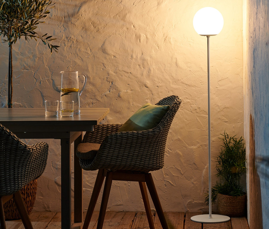 Zwei LED-Akku-Stehleuchten beleuchten eine Terrasse mit Holztisch und Korbstühlen.