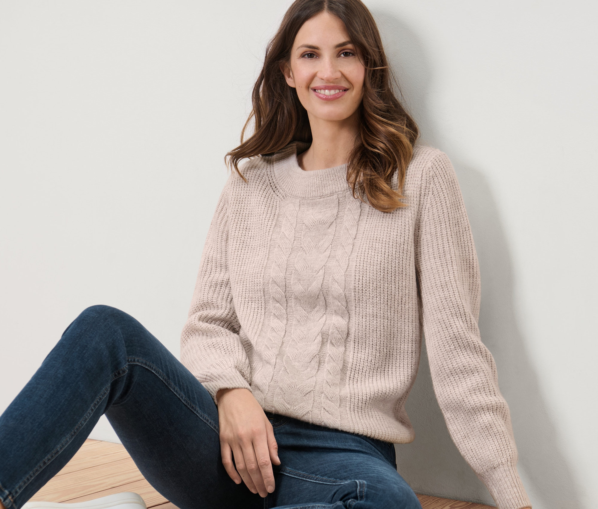 Frau sitzt auf dem Boden und trägt einen Grobstrickpullover mit Zopfmuster.