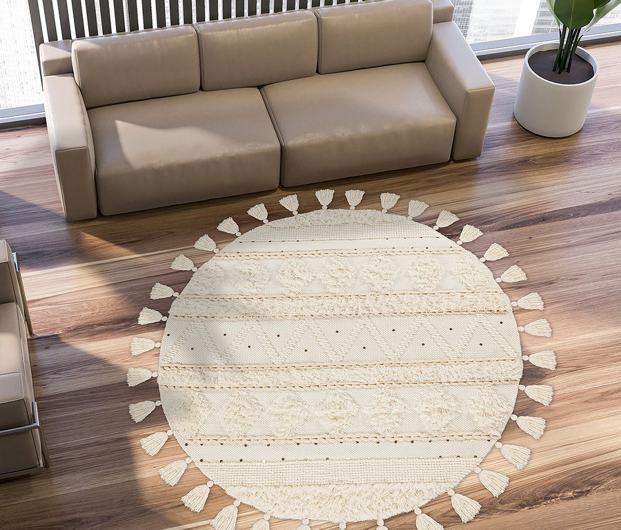 Draufsicht auf ein beiges Sofa, Sessel und einen runden Kayoom Bohist Teppich mit Fransen auf einem Holzboden.