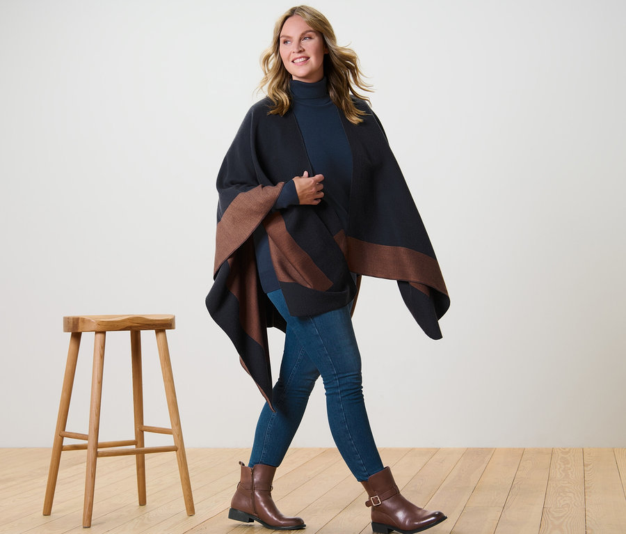 Frau geht, trägt einen Wende-Poncho, einen dunkelblauen Feinstrick-Rollkragenpullover und Jeggings.