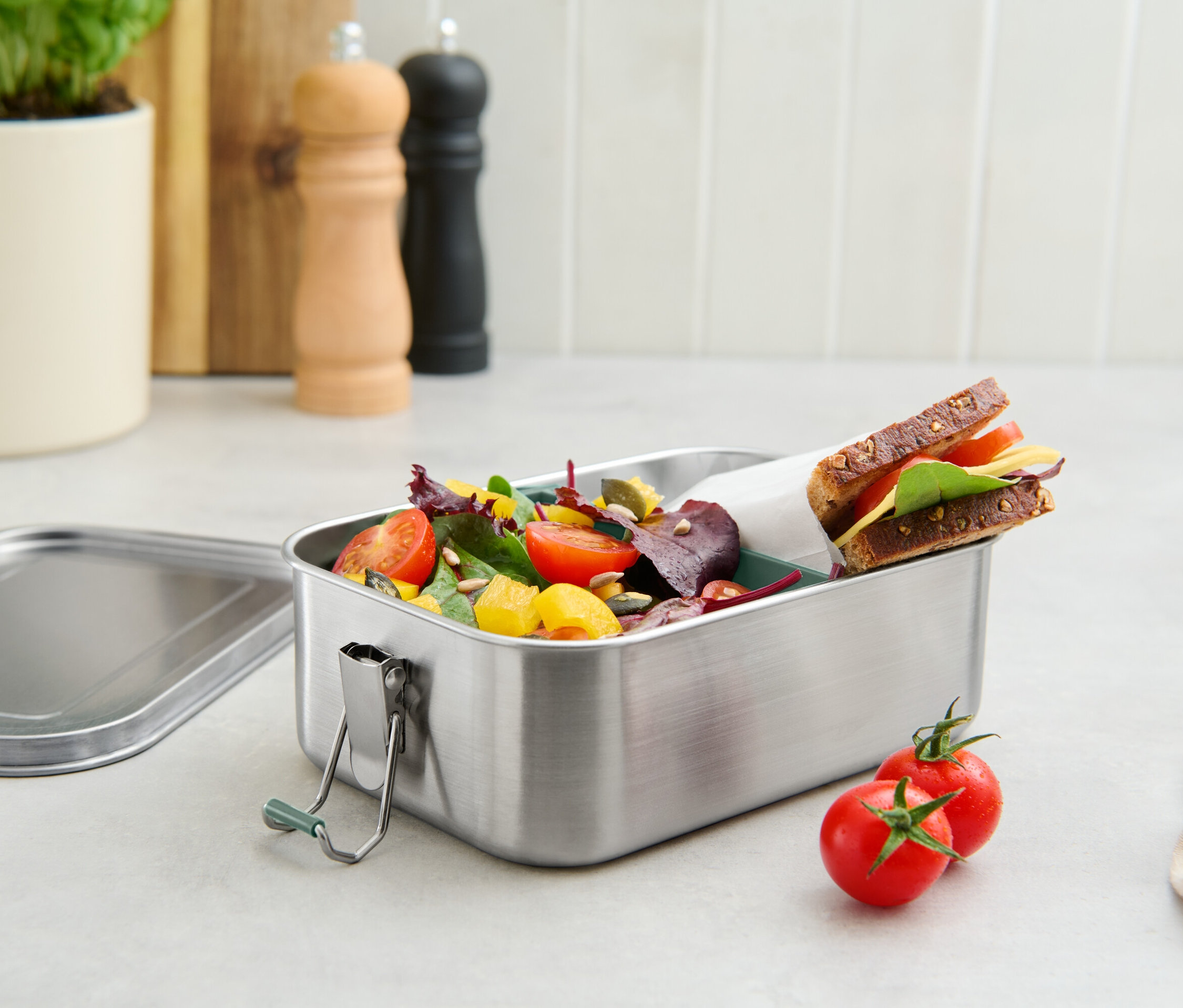 Eine Edelstahl-Lunchbox gefüllt mit Tomaten, Salat und einem Sandwich.