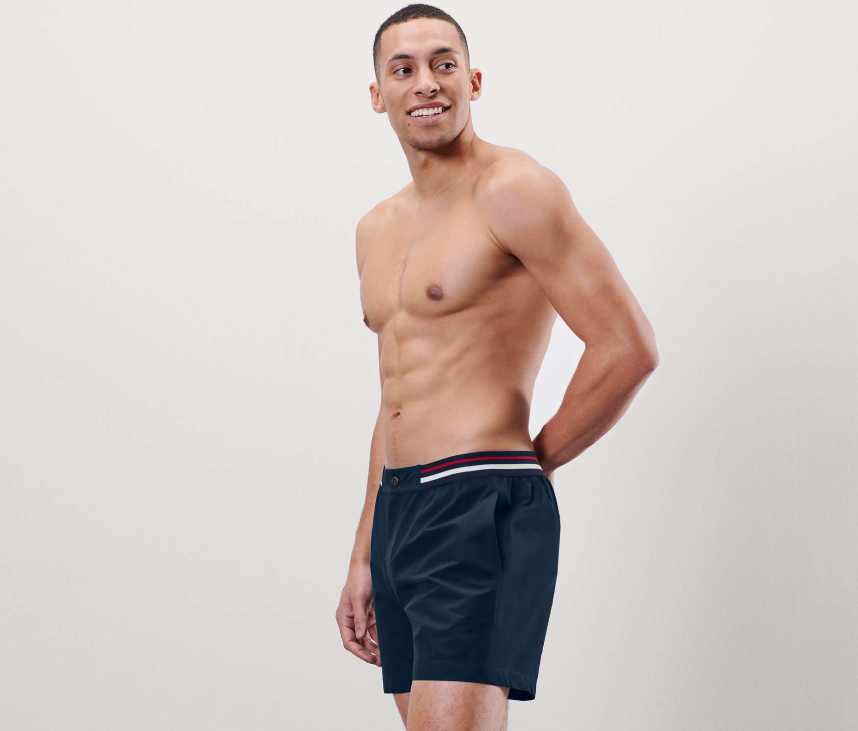 Mann posiert ohne Hemd in Badeshorts.