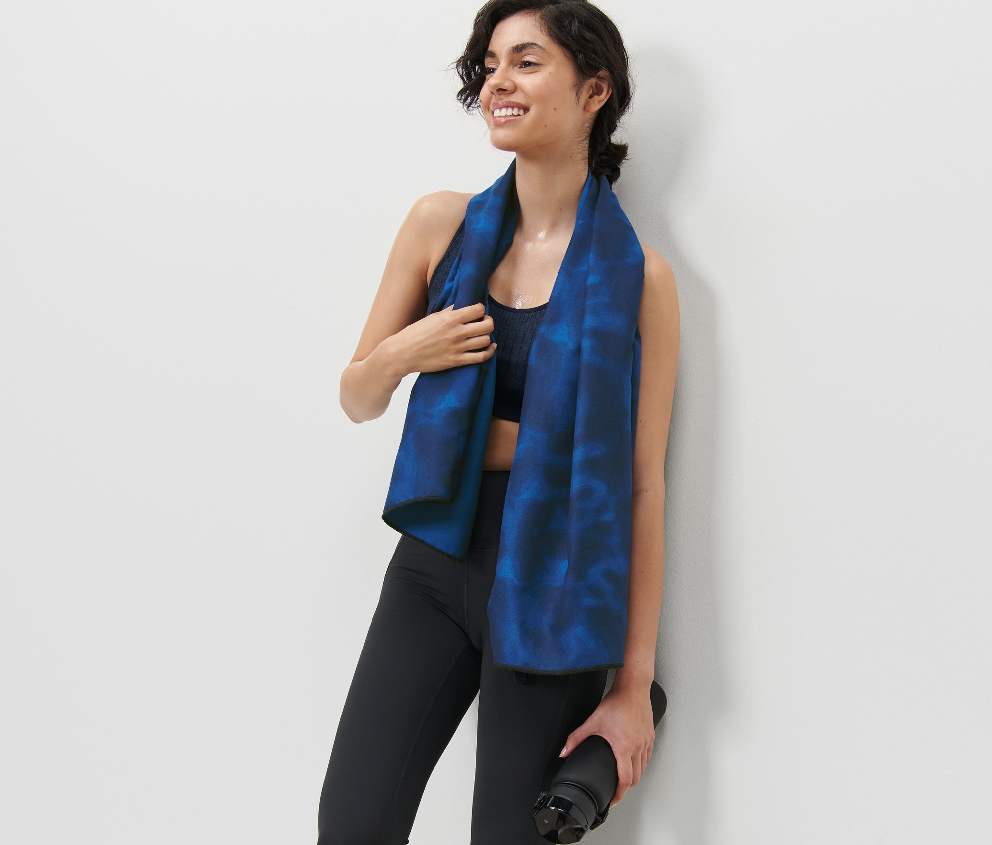 Frau trägt ein Sporthandtuch und hält eine Wasserflasche.