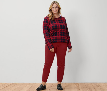 Eine Frau steht und trägt ein kariertes Blusenshirt, eine rote Stretchhose und Leder-Loafer.