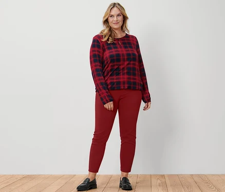 Eine Frau steht und trägt ein kariertes Blusenshirt, eine rote Stretchhose und Leder-Loafer.