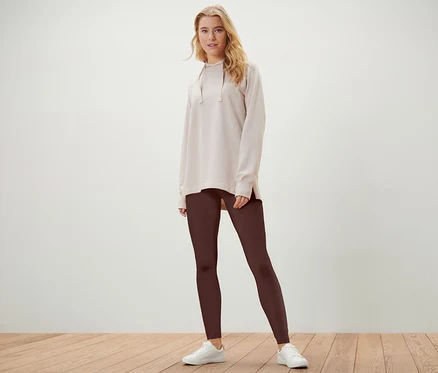Blonde Frau posiert in hellbeigem Hoodie und braunen 2 Leggings.