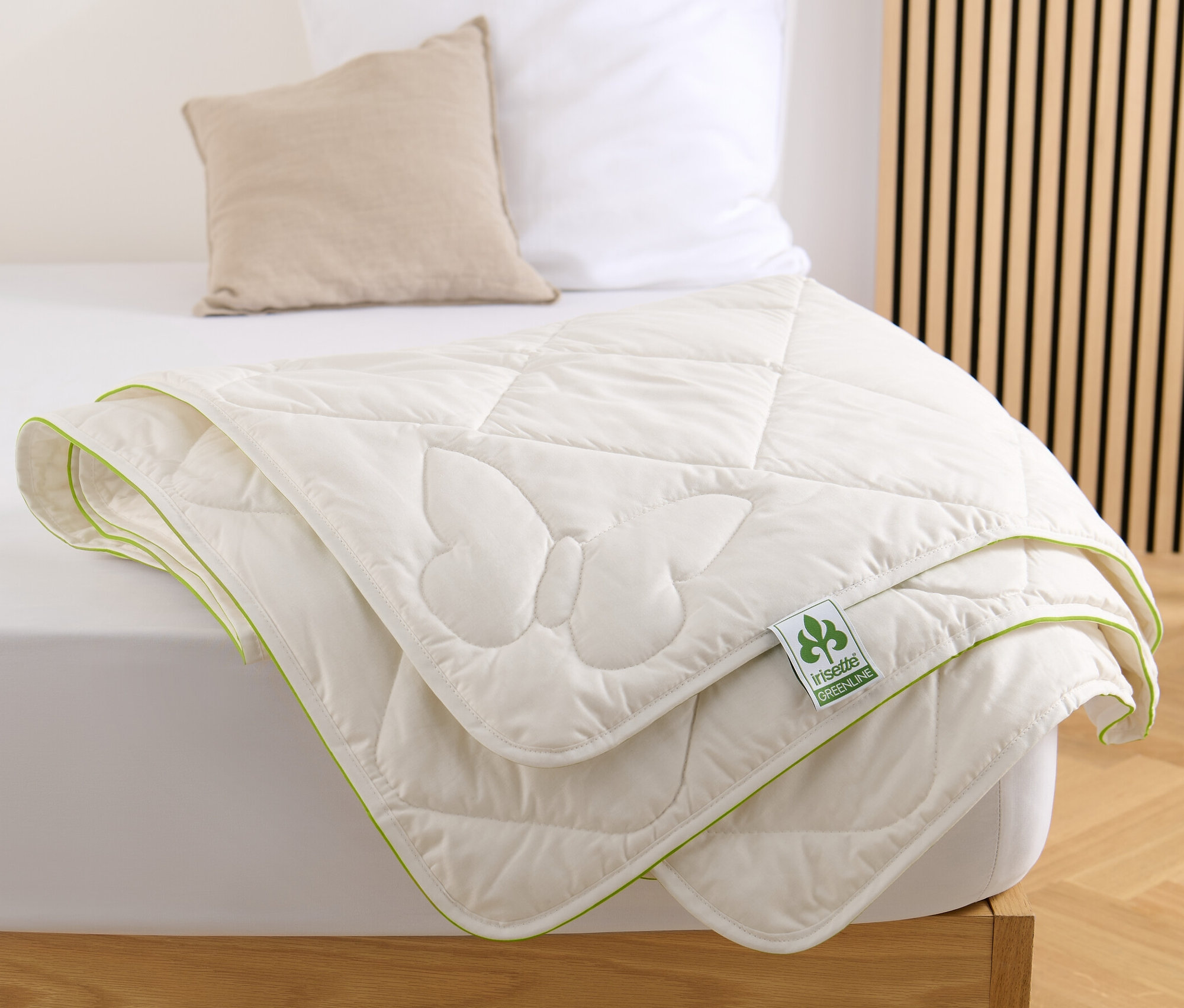 Eine weiße irisette® greenline Seiden-Baumwollbett mit Schmetterlingsmuster und grüner Bordüre liegt auf einem Bett.