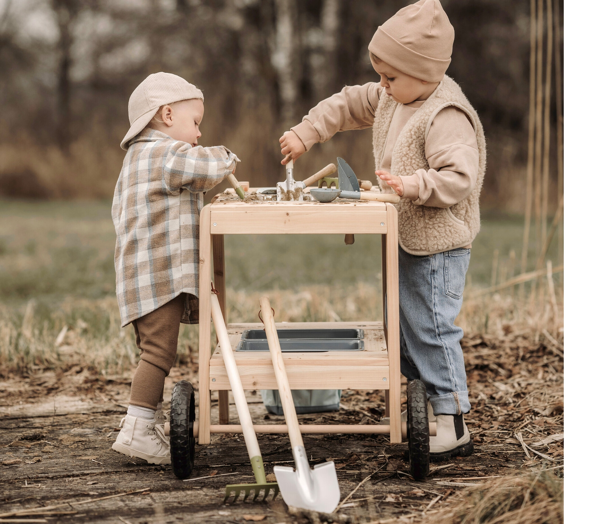 Zwei Kleinkinder spielen mit der small foot Matschküche kompakt und dem großen Gartenwerkzeug-Set.
