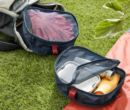 Auf dem Gras liegen ein offener Rucksack und zwei Rucksack-Organizer. Ein Organizer ist mit roter Kleidung gefüllt.