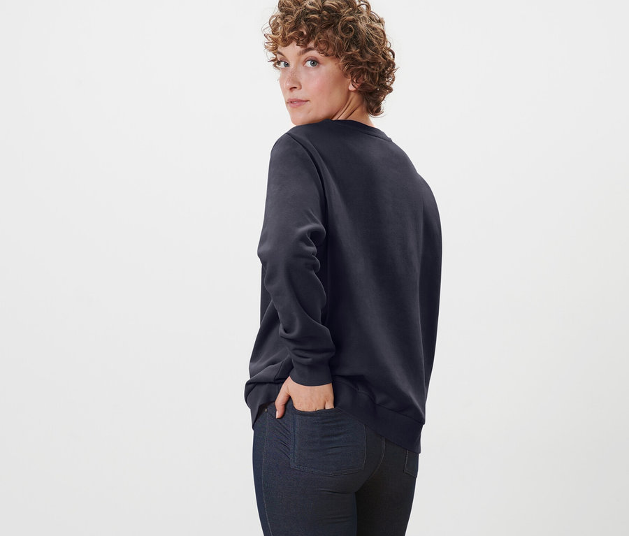 Frau blickt über die Schulter und posiert in dunkelblauem Sweatshirt.