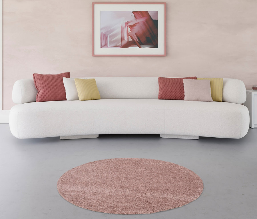 Ein pinker Teppich »Charme« (ca. 120 cm) liegt vor einem weißen Sofa im Wohnzimmer.