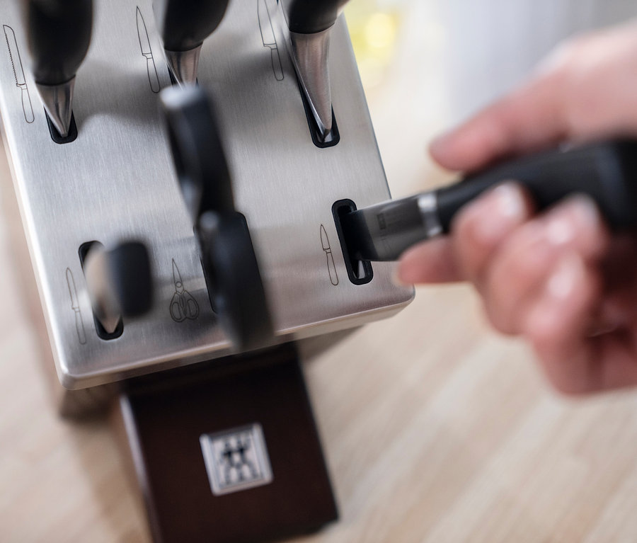 Eine Hand legt ein Messer in den ZWILLING **** VIER STERNE Selbstschärfender Messerblock, 6-tlg.