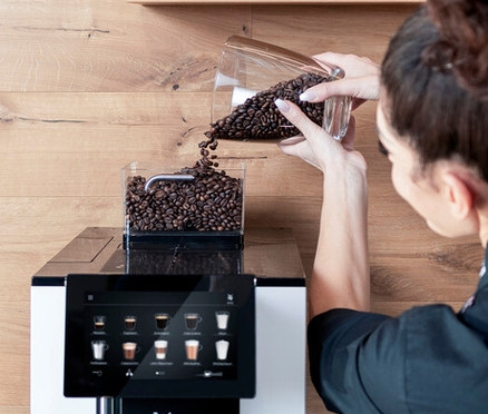 Frau füllt Kaffeebohnen in einen Profi-Kaffeevollautomat »WMF 950 S«.