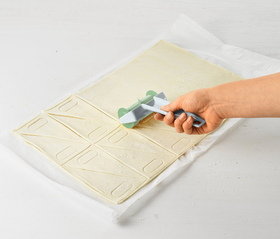 Eine Hand benutzt einen Croissant-Roller, um Teig in Dreiecke zu schneiden.