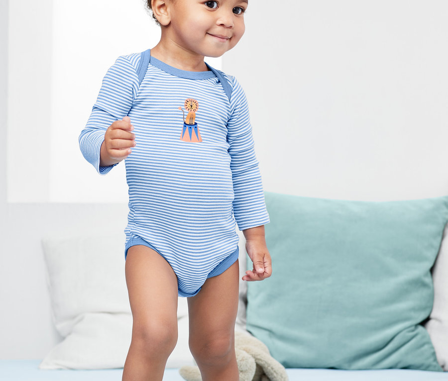 Kleinkind steht auf einem Bett und trägt einen blau-weiss gestreiften Langarmbody. Das Kind trägt einen von 3 Langarm-Bodys.
