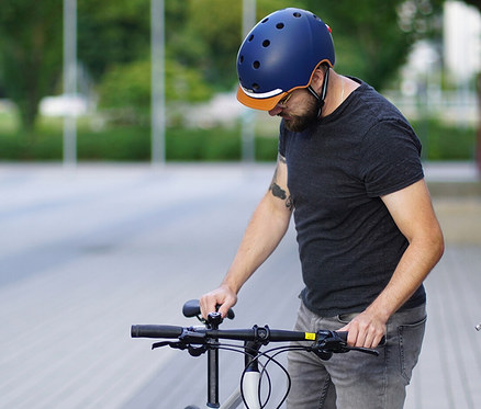 Mann mit Bart steht neben einem Fahrrad und trägt einen blauen Melon E-Series Fahrradhelm »Heaven & Earth«.